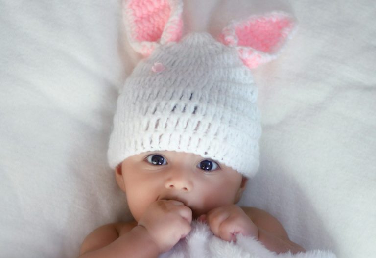 baby in white knit cap lying on white textile